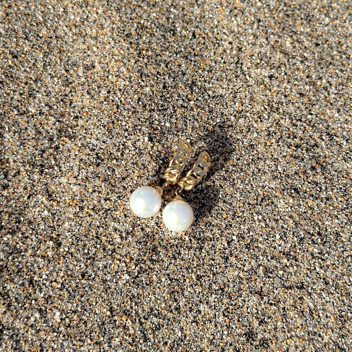 argollas de oro con perlas sobre arena playa